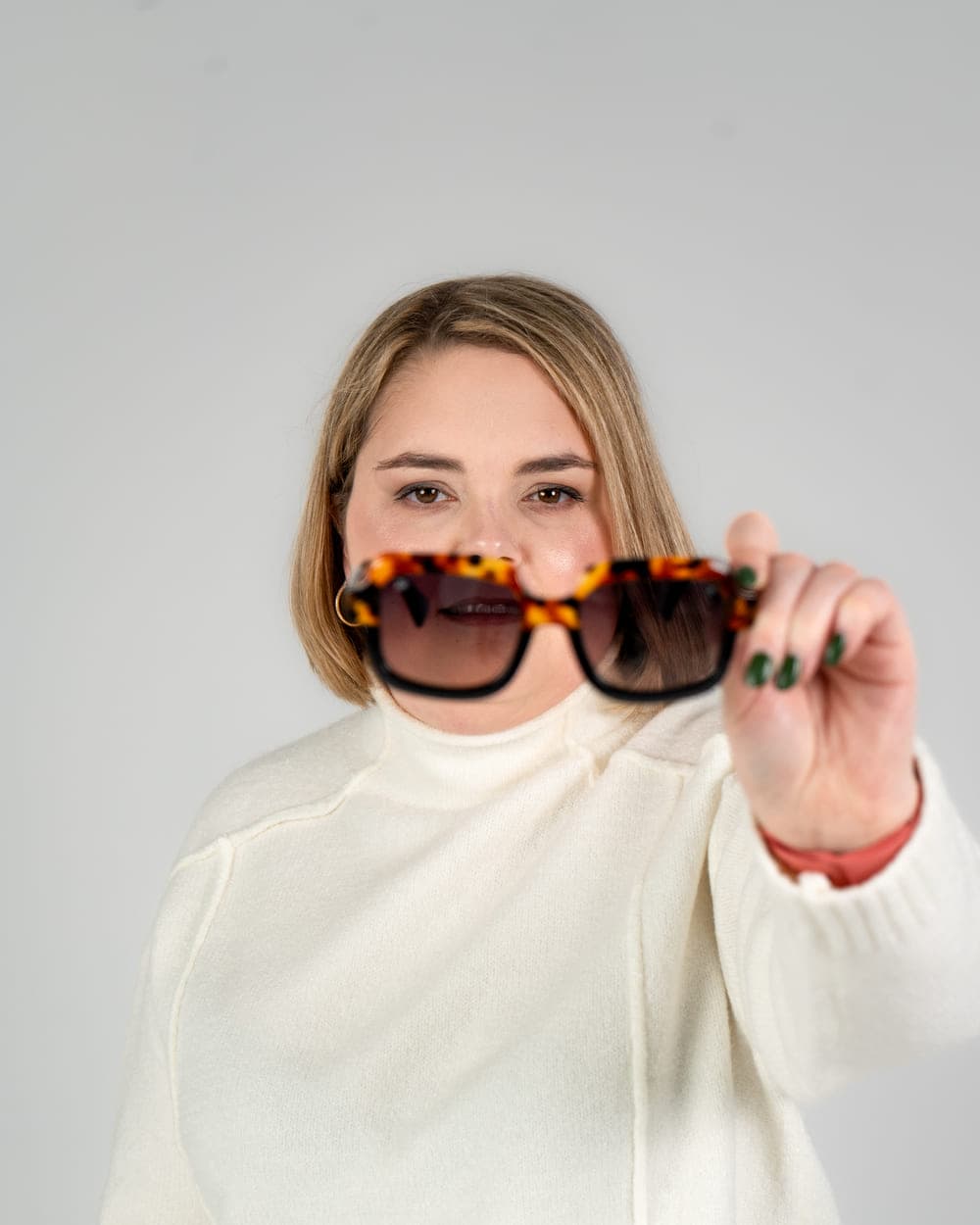 Sabrina tient une paire de lunettes de soleil écaille devant l'objectif, souriant derrière.